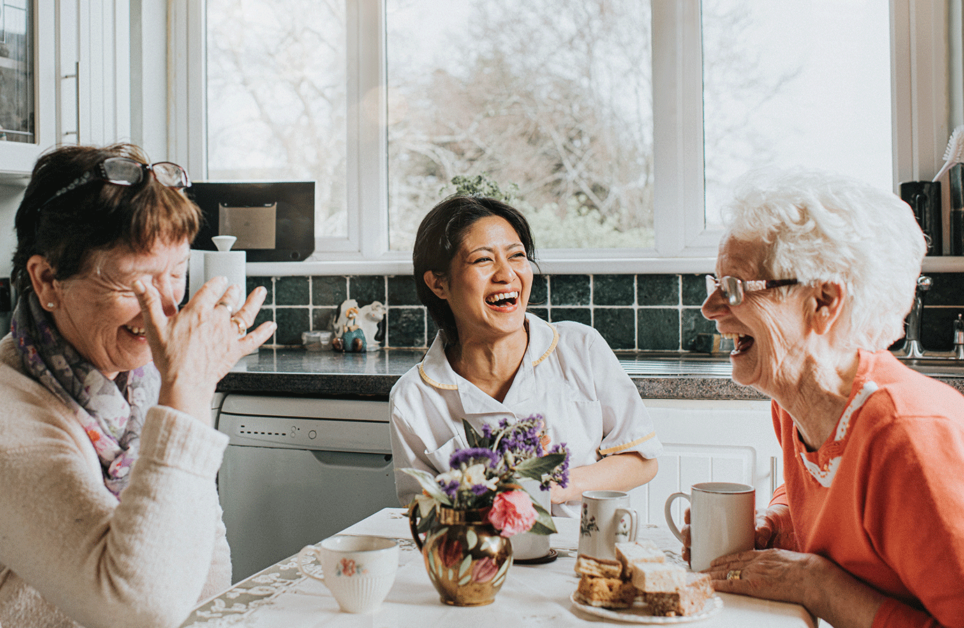 seniors and caregiver sitting at kitchen table and laughing