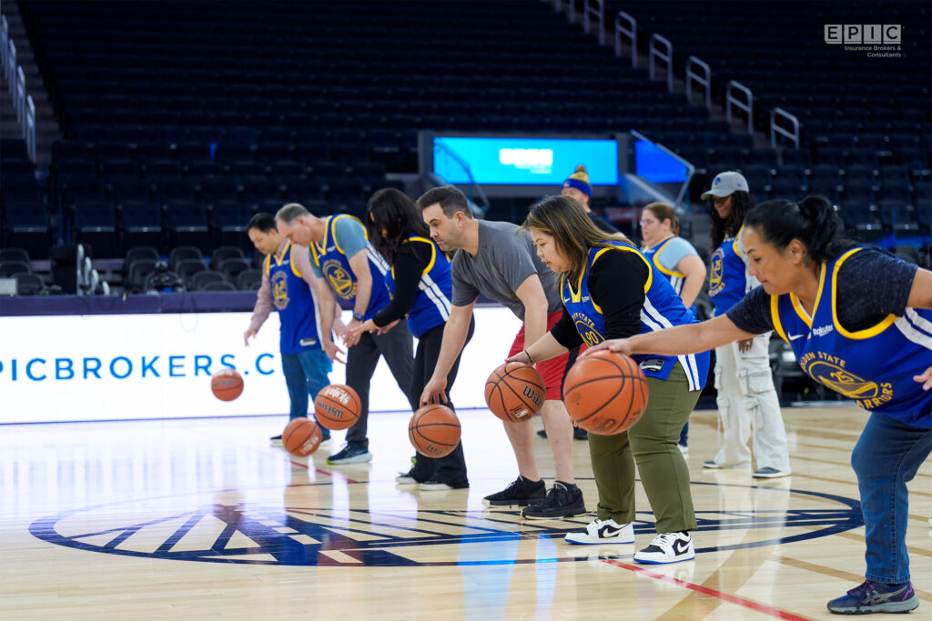 A group of people in Golden State Warriors jerseys practicing basketball dribbling on a court with 